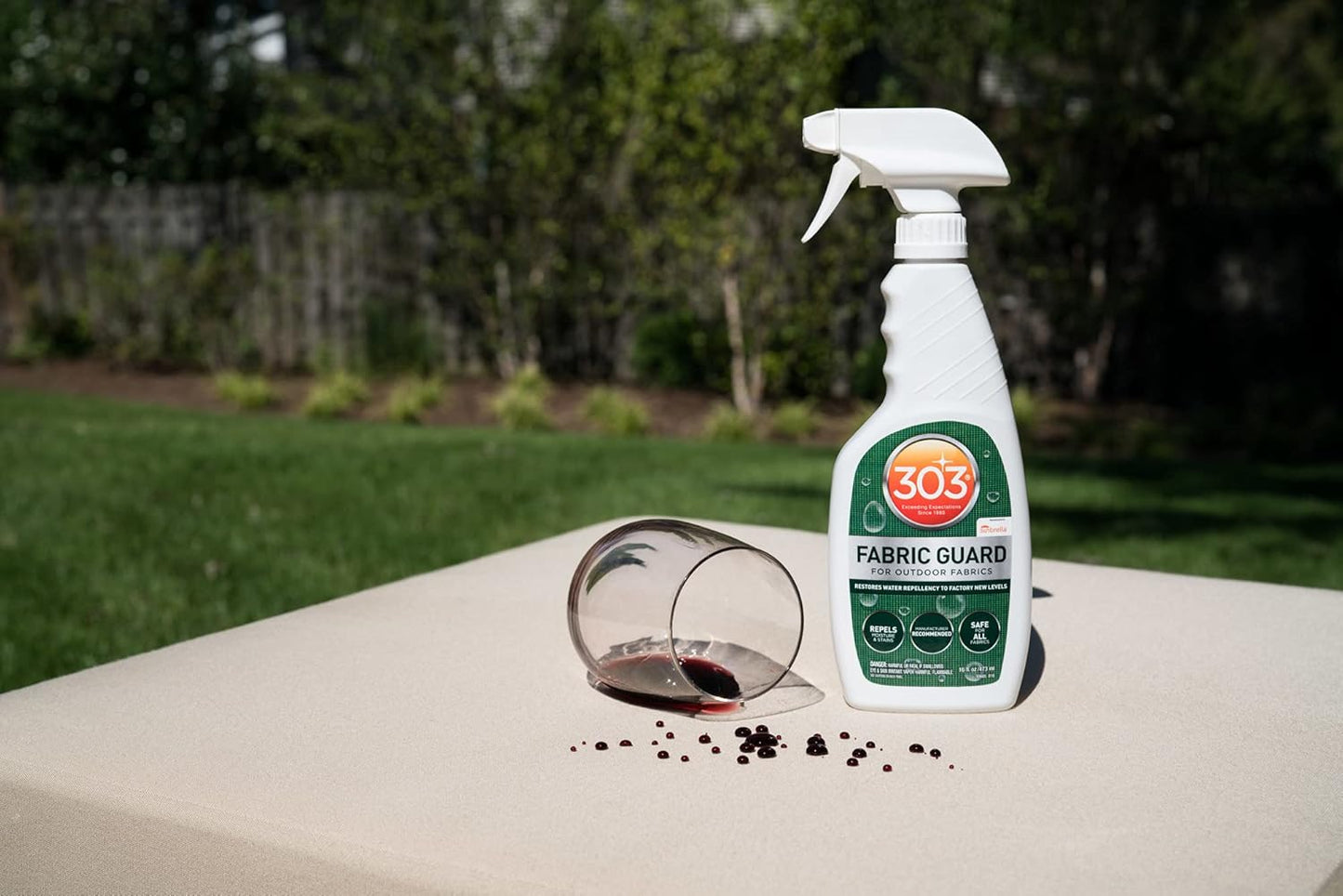 A 16oz bottle of Pool Goods 303 Fabric Guard for Outdoor Fabrics (Sunbrella) sits next to spilled red wine on beige outdoor fabric, demonstrating its safe, powerful protection against stains and moisture.