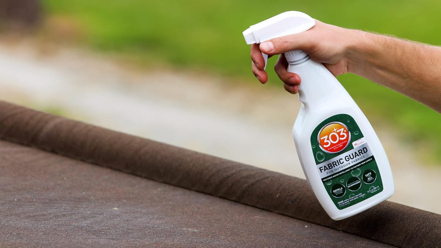 A hand holds a bottle of Pool Goods 303 Fabric Guard for Outdoor Fabrics (Sunbrella) 16oz over brown outdoor fabric, showing its stain and moisture protection, with a blurred green background.
