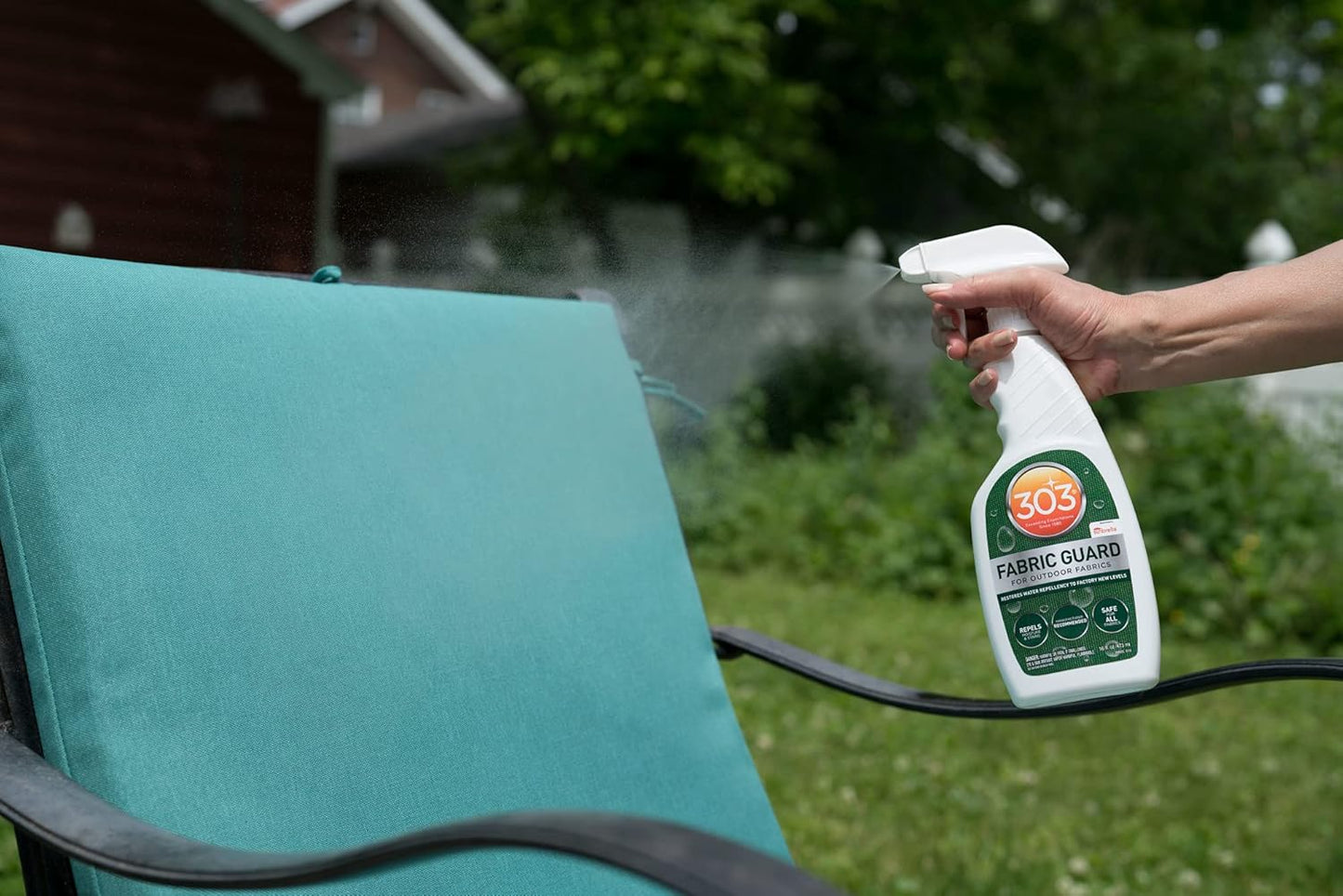 A hand applies Pool Goods 303 Fabric Guard for Outdoor Fabrics (Sunbrella) 16oz onto a teal chair cushion outdoors, repelling moisture and guarding against stains.
