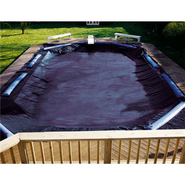 A Swimline Deluxe 16' x 24' Rectangle Winter Cover in blue/black protects the above-ground pool, which is bordered by a wooden deck and railings.