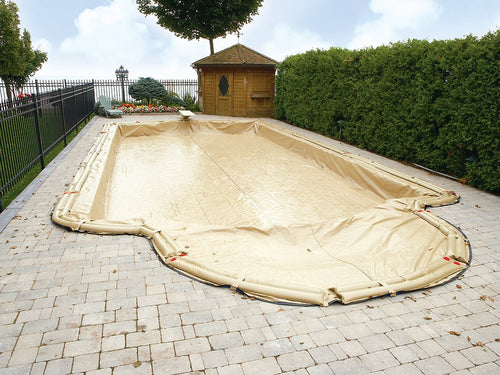 A rectangular swimming pool is covered with a green safety cover secured with straps and springs to the surrounding concrete deck.