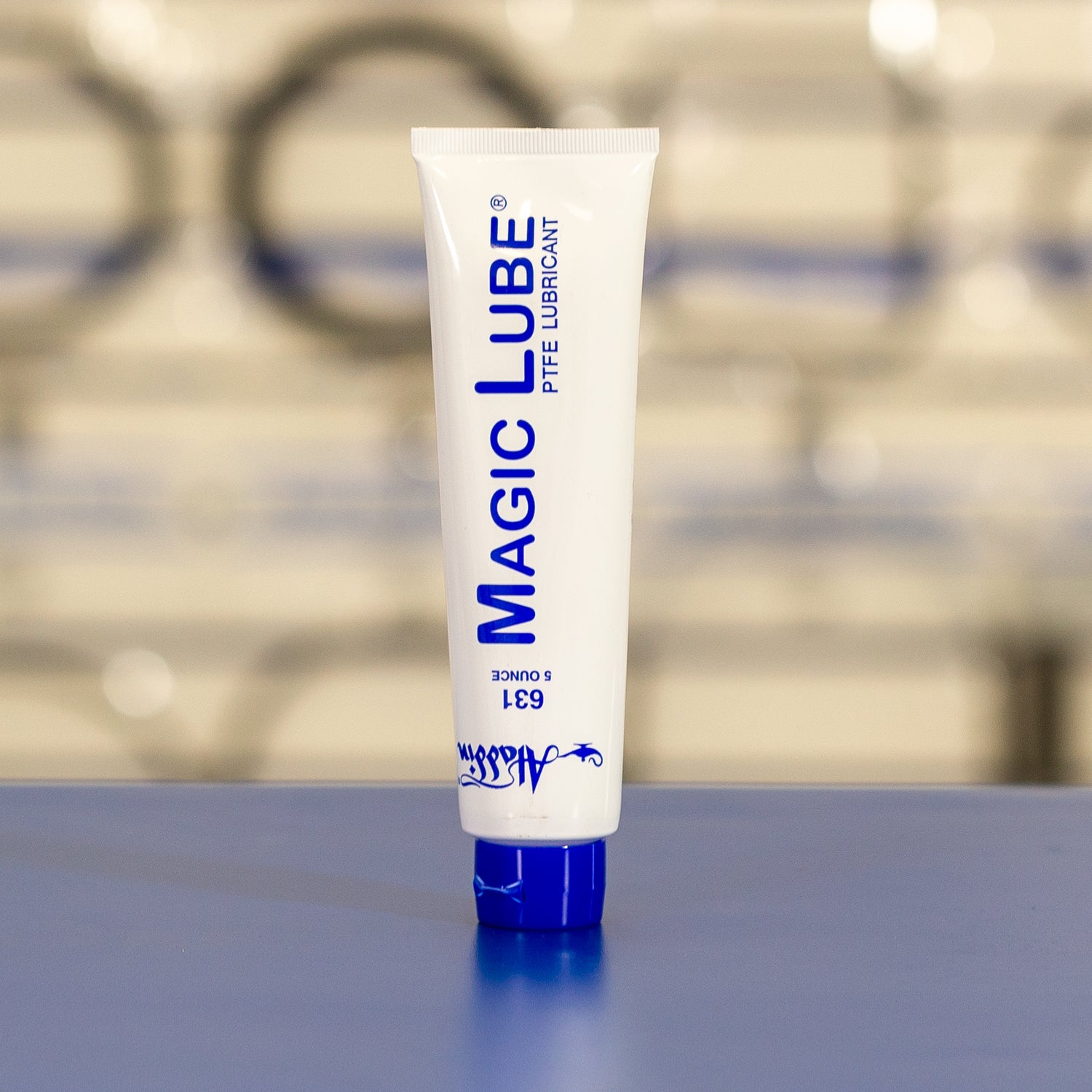 A 5 oz Aladdin Magic Lube Teflon Lubricant tube, by MagicLube, with blue text on a white background rests smoothly on a surface, suitable for wet and dry environments, against a blurred backdrop.