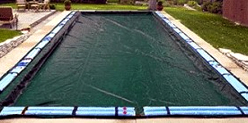 A 16' x 32' rectangular pool is covered with a SWIMLINE CORP. RE RIPSTOPPER COVER, secured by blue water bags, and surrounded by grass and a patio area.